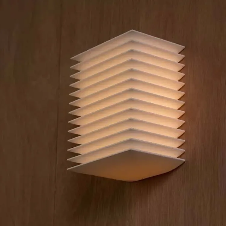 Applique Hotaru allumée, lamelles blanches superposées sur un mur en bois