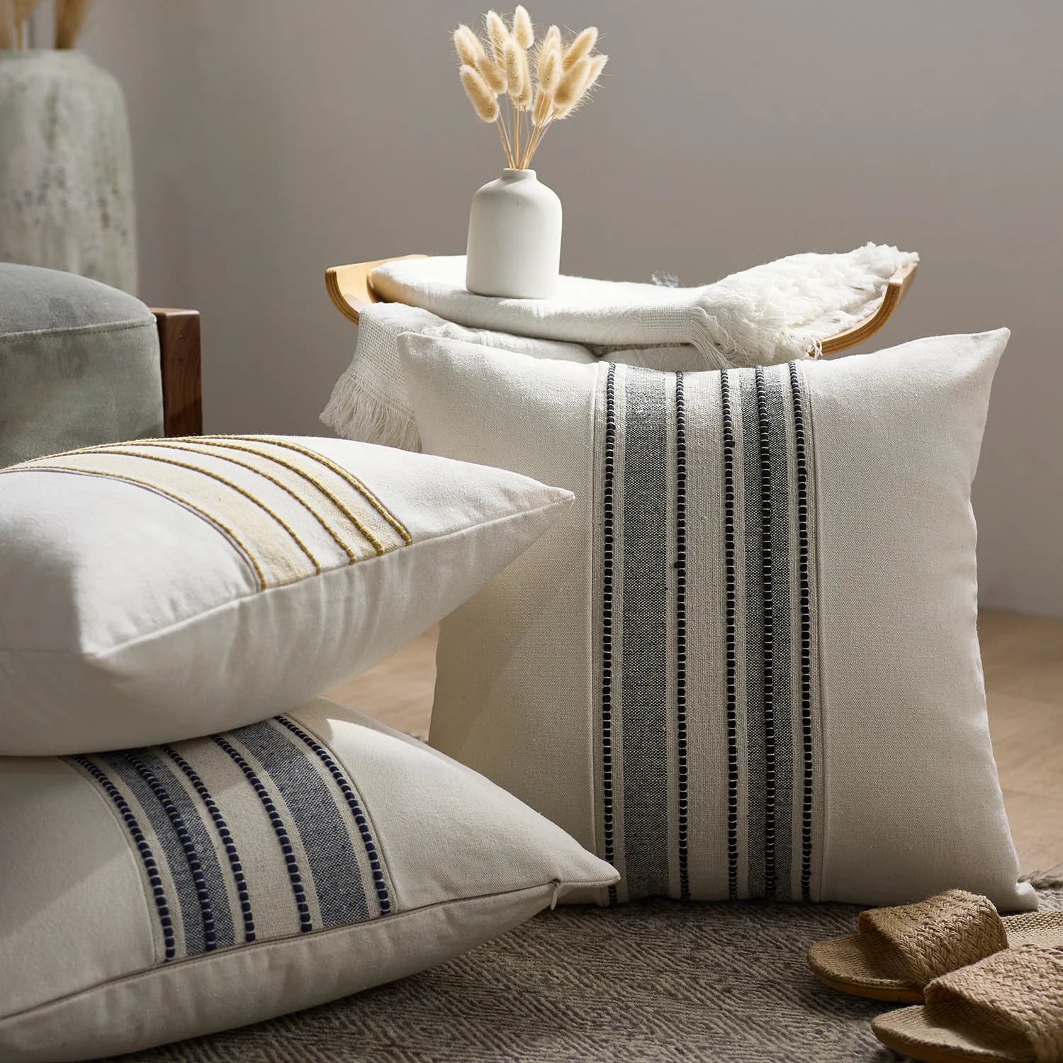 Housses de coussin Shima écrues à rayures tissées, posées sur un tabouret près d'un plaid
