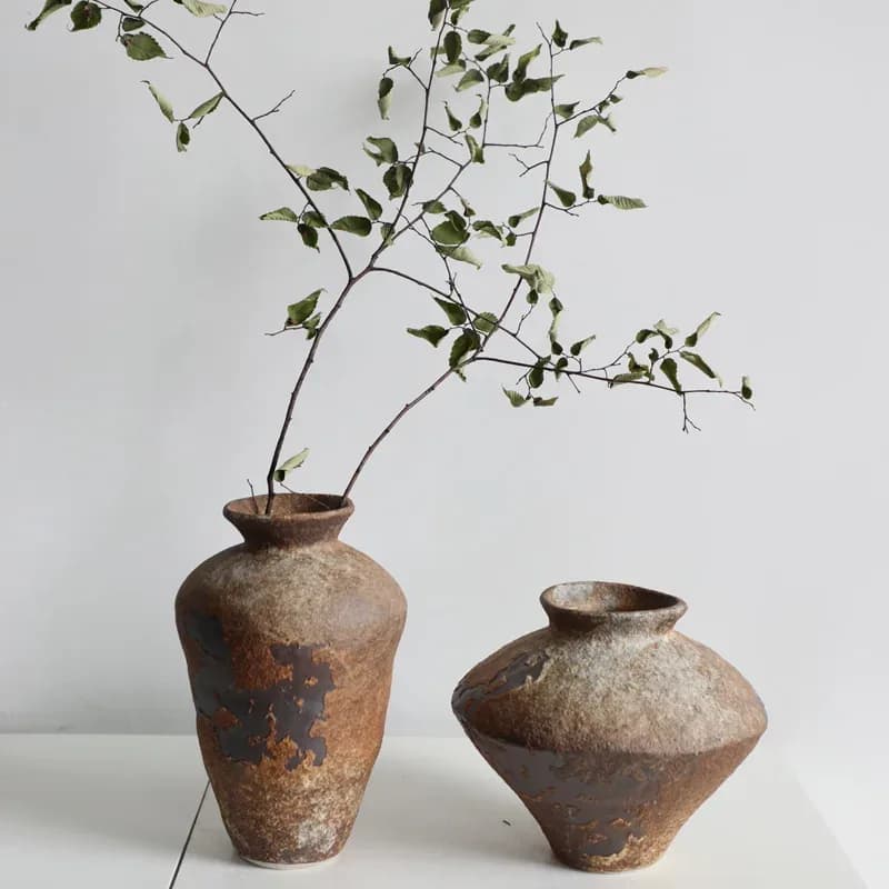 Deux vases Kage en céramique brute aux teintes rouille, l'un garni de branchages
